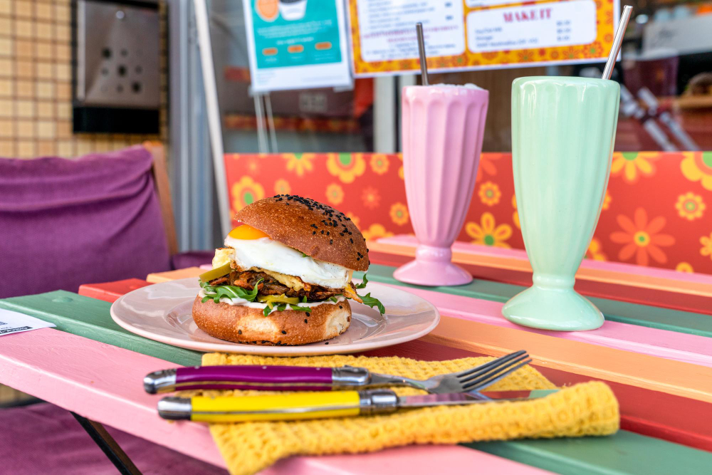 Tasty burger with eggs on a pink plate with glasses of milkshakes