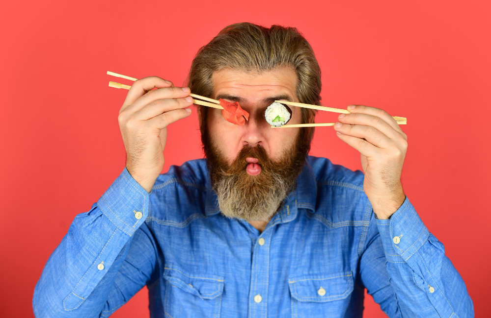 A man eating sushi chopsticks while joking