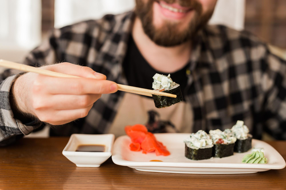 A man eating sushi rolls using bamboo sticks